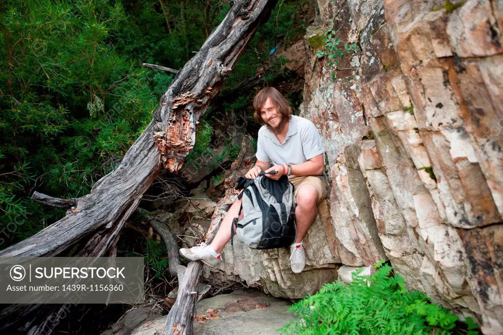 Portrait of young male hiker photographing sitting on rock