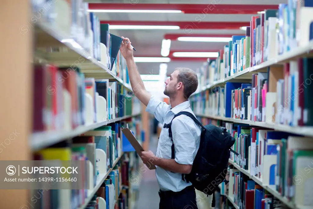 Young man holding clipboard in library