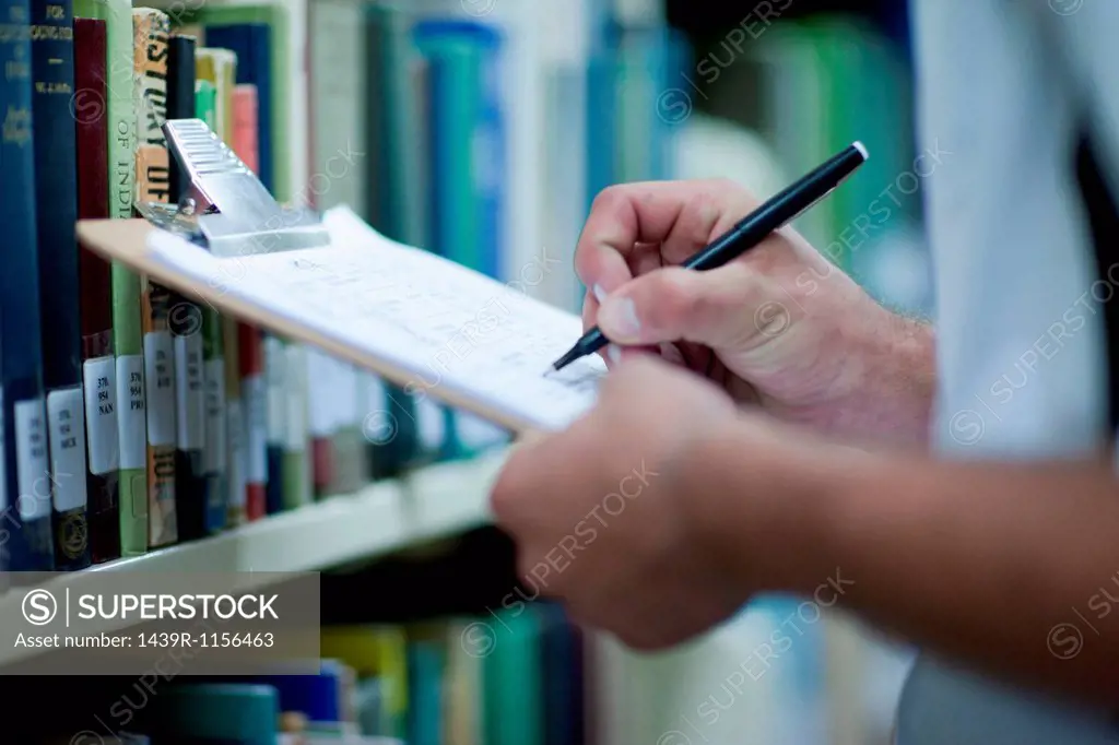 Young man writing on clipboard in library
