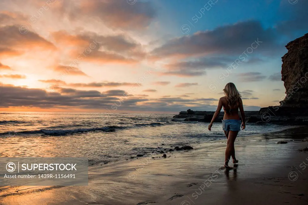 Young woman walking on beach at sunset, rear view