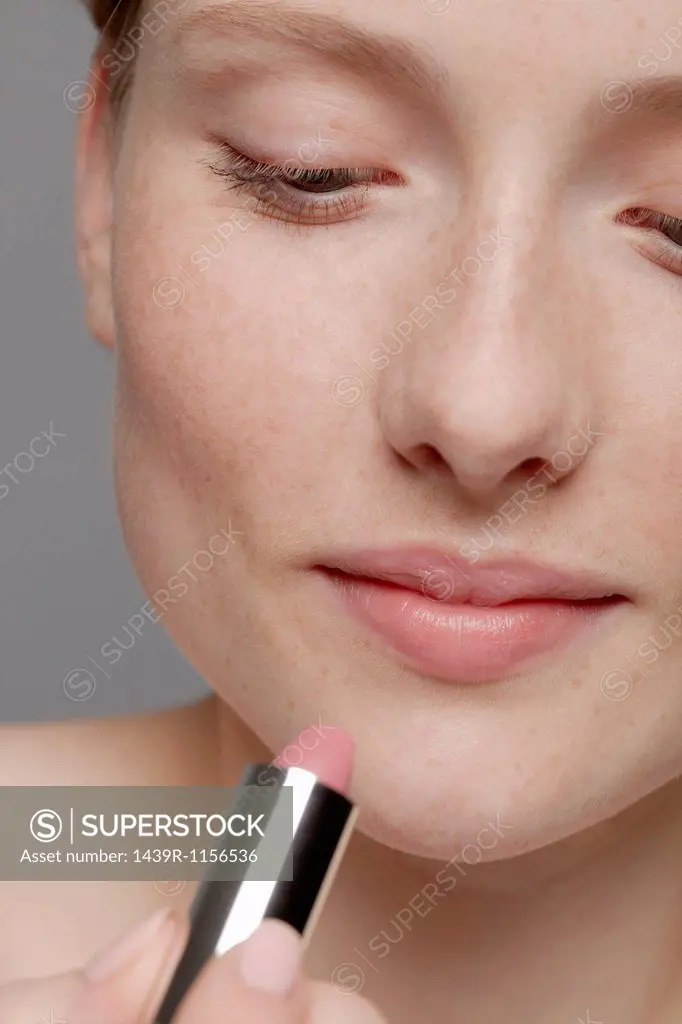 Close up of part of young woman´s face, applying lipstick