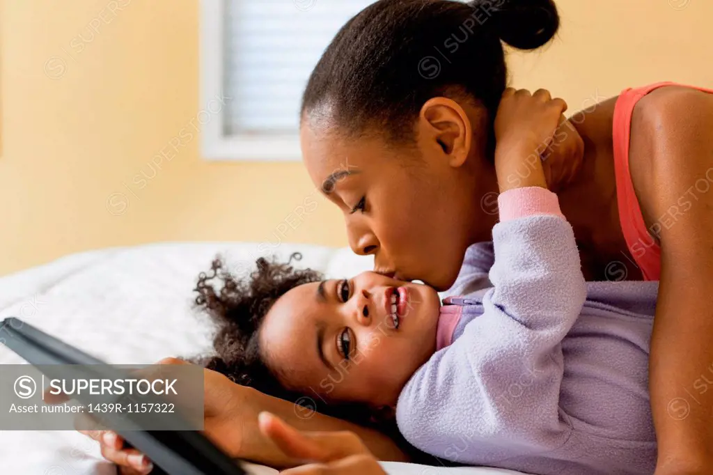 Mother kissing daughter and holding digital tablet