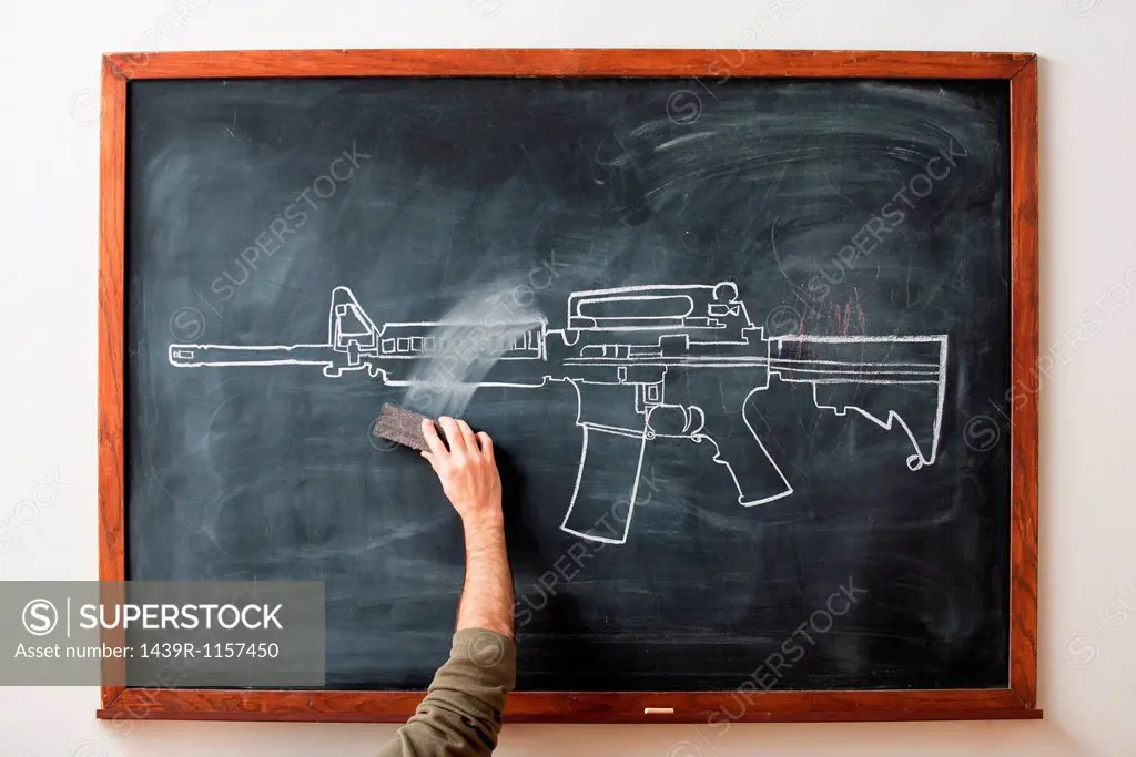 Person erasing chalk drawing of gun on blackboard