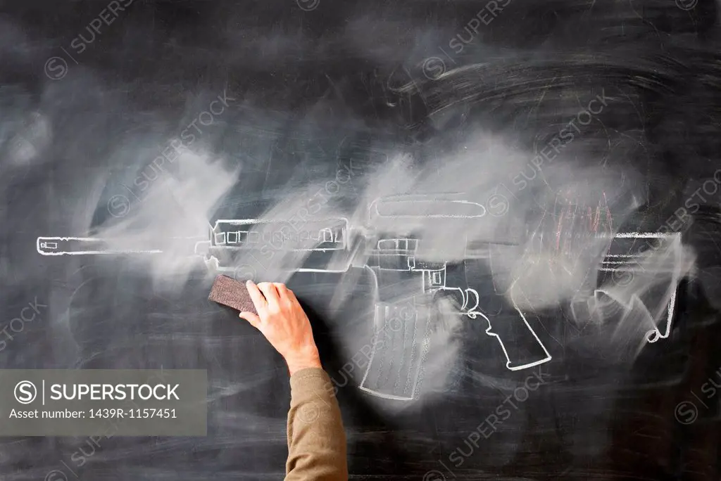 Person erasing chalk drawing of gun on blackboard