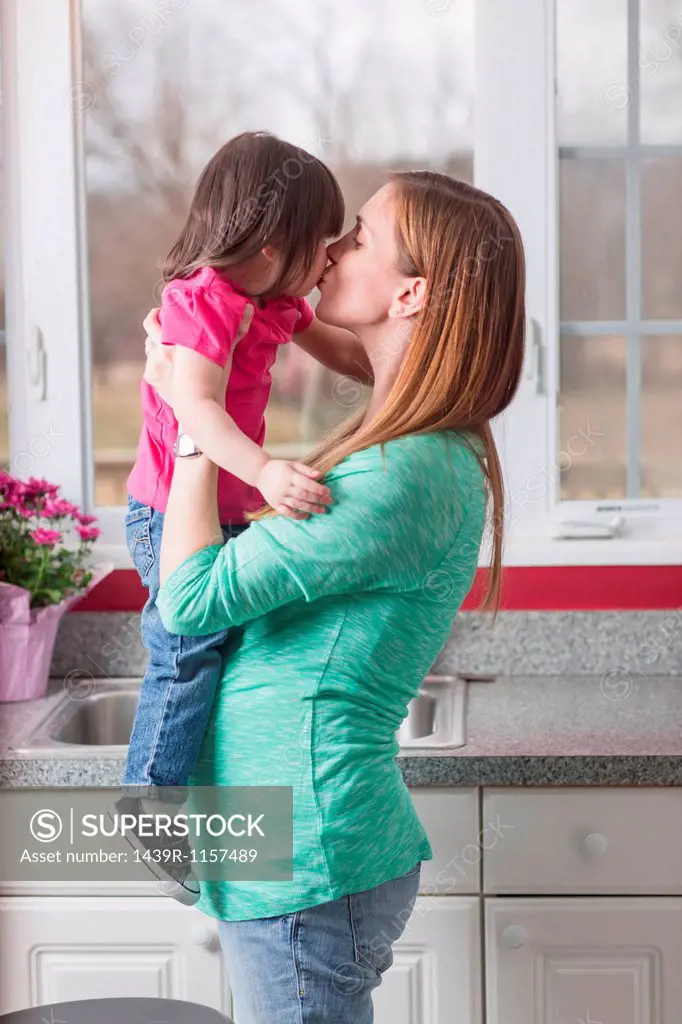 Pregnant mother holding toddler daughter in kitchen
