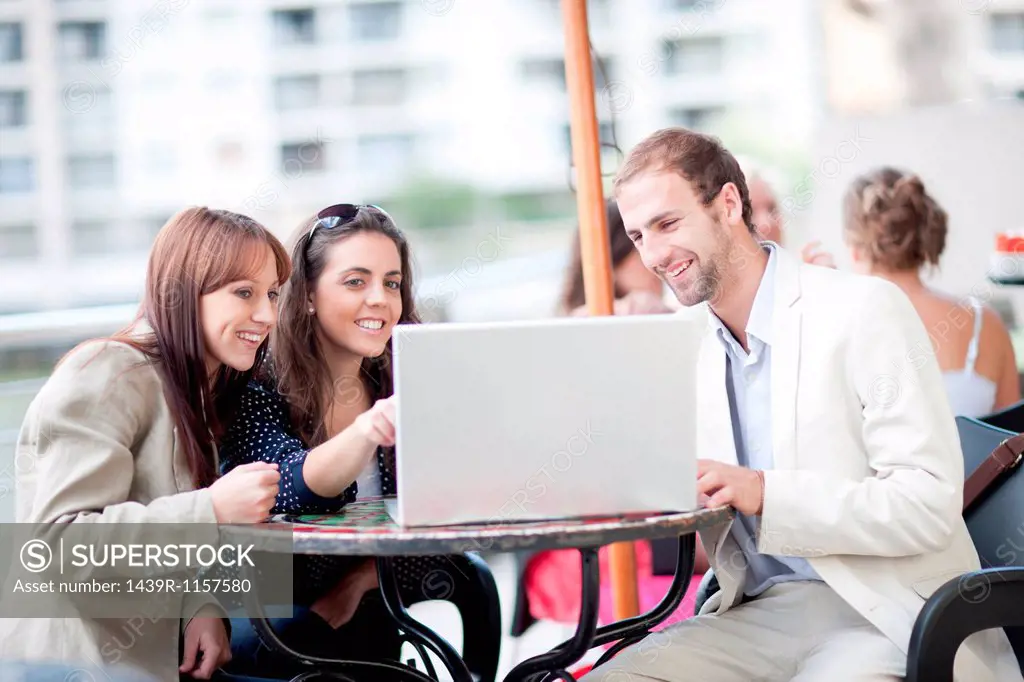 Young women and young man using laptop in cafe