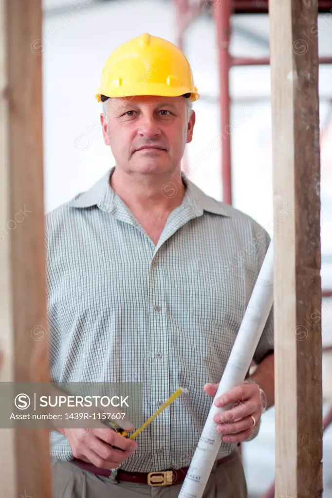 Portrait of a builder with tape measure and blueprint on construction site