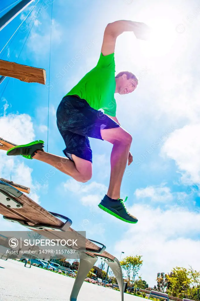Young man leaping over park bench in city
