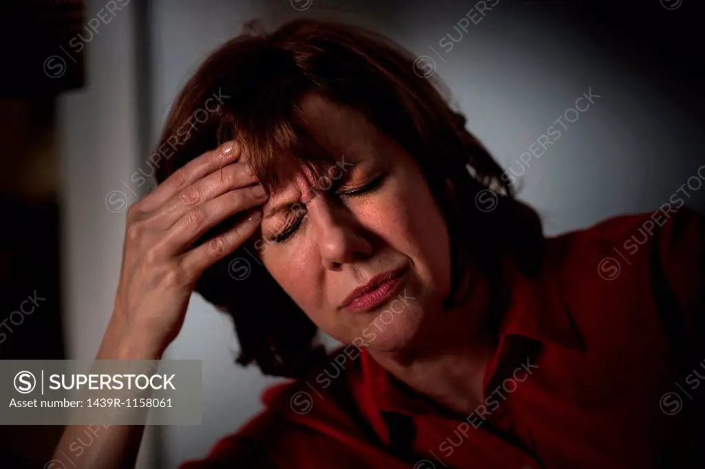 Mature woman with hand on head and eyes closed