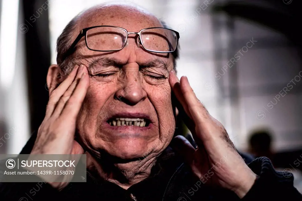 Senior man with eyes closed, wearing glasses, looking stressed