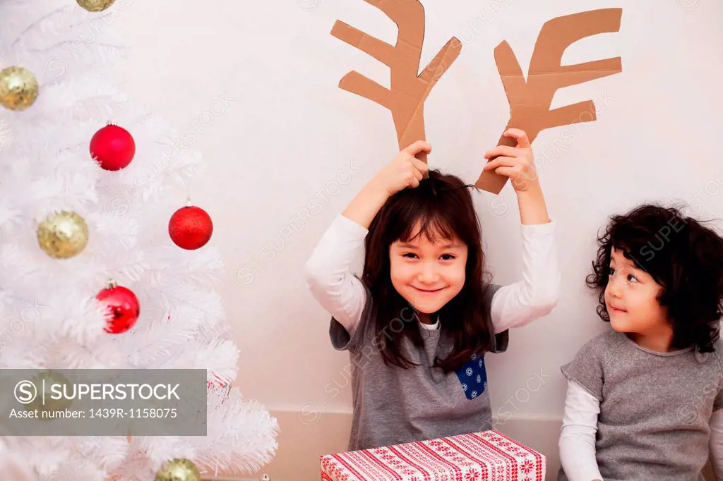 Two girls preparing for Christmas, playing with cardboard reindeer antlers