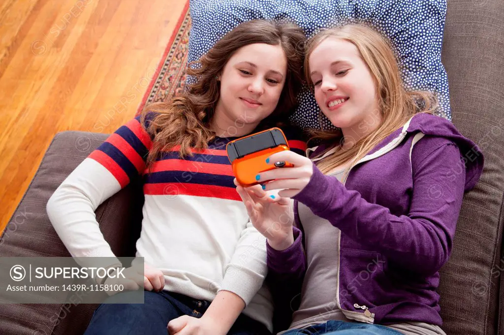 Girls lying on sofa playing handheld video game