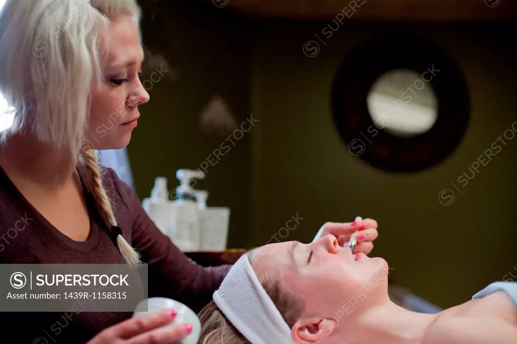 Beautician performing facial on woman, lying with eyes closed