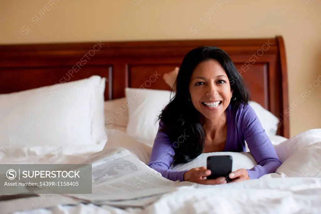 Mature woman lying on bed holding mobile phone, portrait