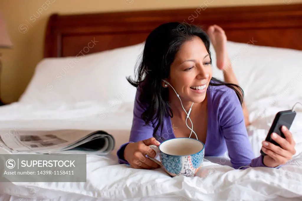Mature woman lying on bed and listening to mp3 player, smiling