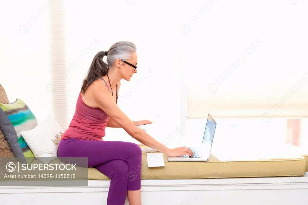 Woman sitting on window seat using laptop