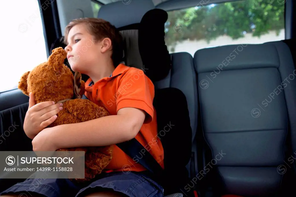 Boy looking out of car window holding teddy bear