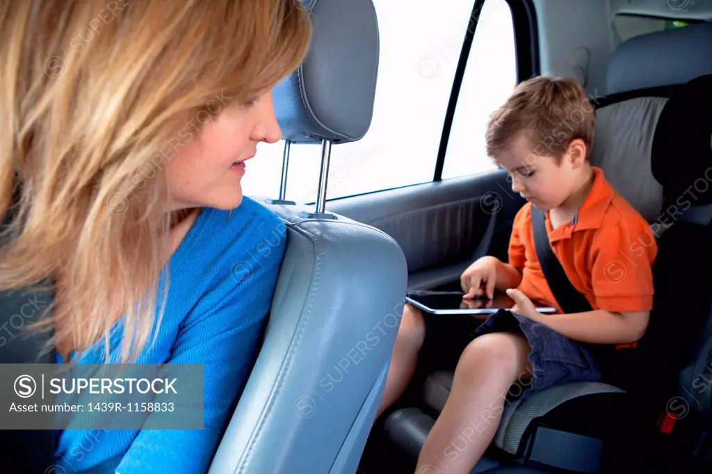 Mother watching son use digital tablet in back seat of car