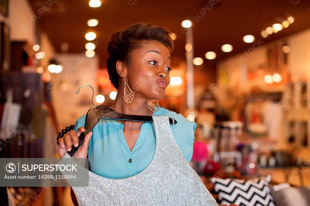 Young woman holding silver top in vintage shop, pouting