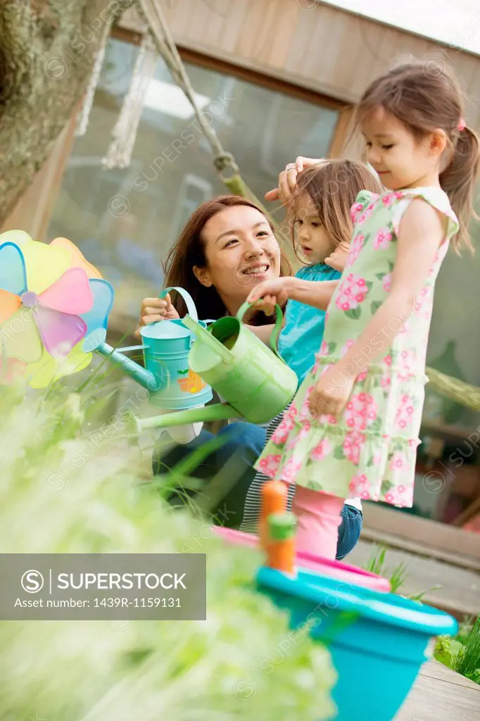Mother and two daughters with toy watering cans in garden