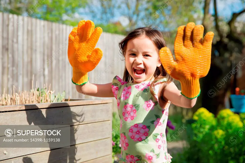 Young girl in garden wearing oversized gloves