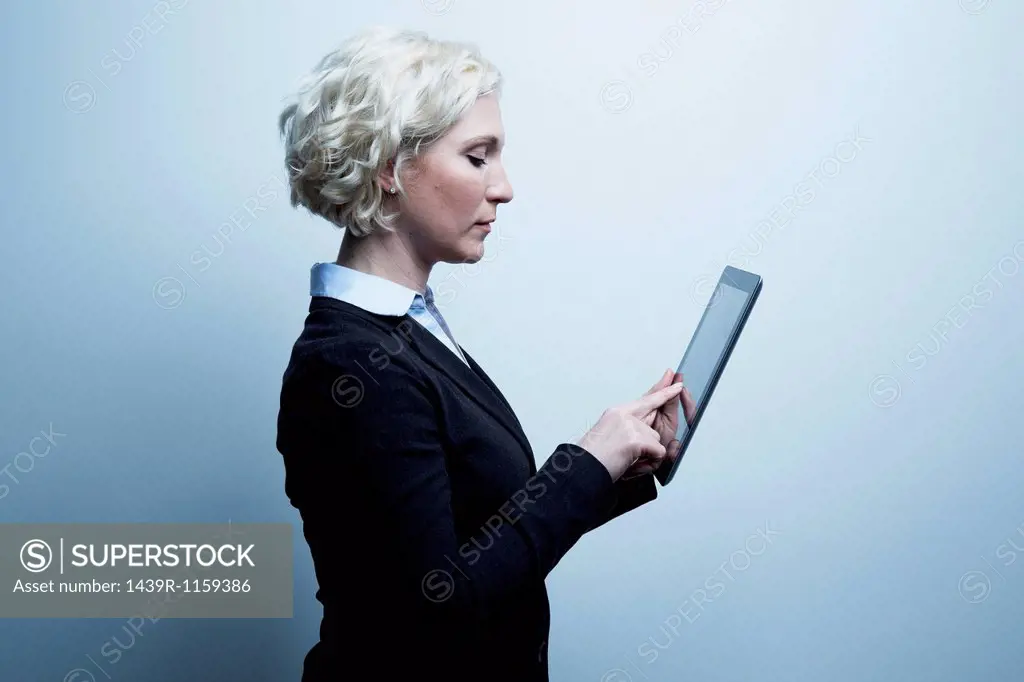 Studio portrait of blond businesswoman looking at digital tablet