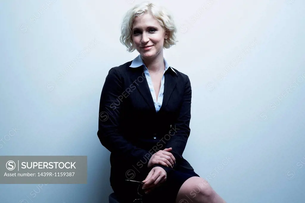 Studio portrait of blond businesswoman sitting on stool