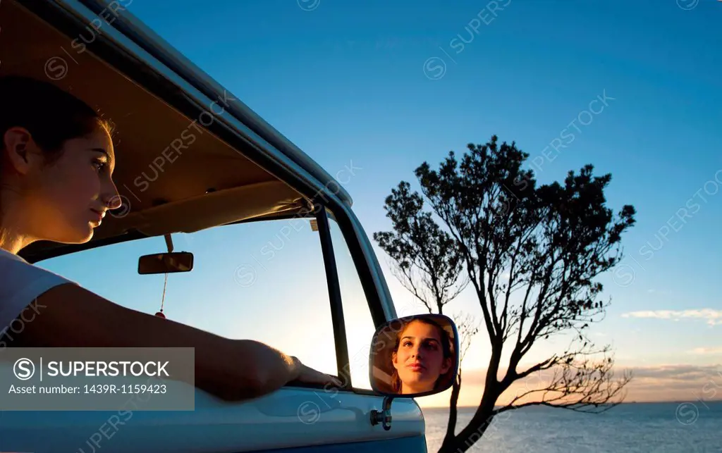 Young woman looking out of camper van window at dusk