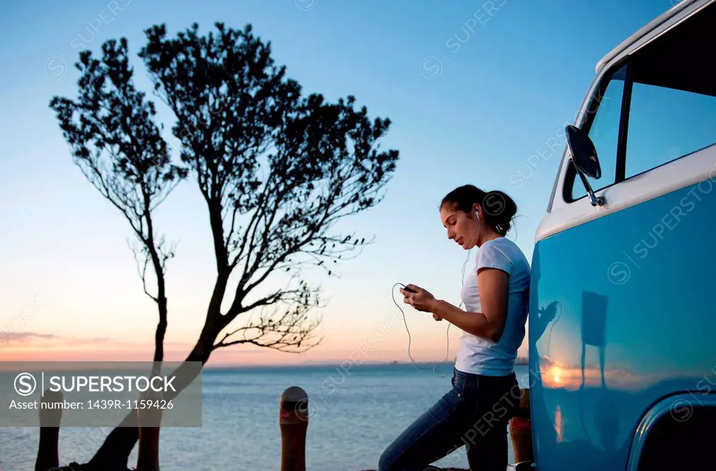 Young woman leaning on camper van at dusk