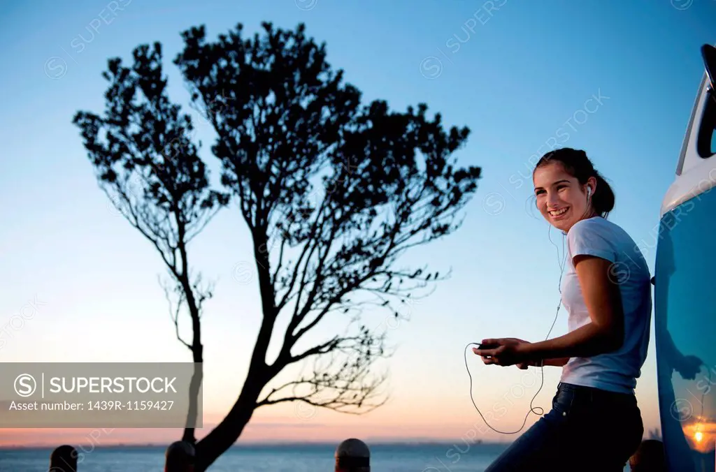 Smiling young woman leaning on camper van at dusk