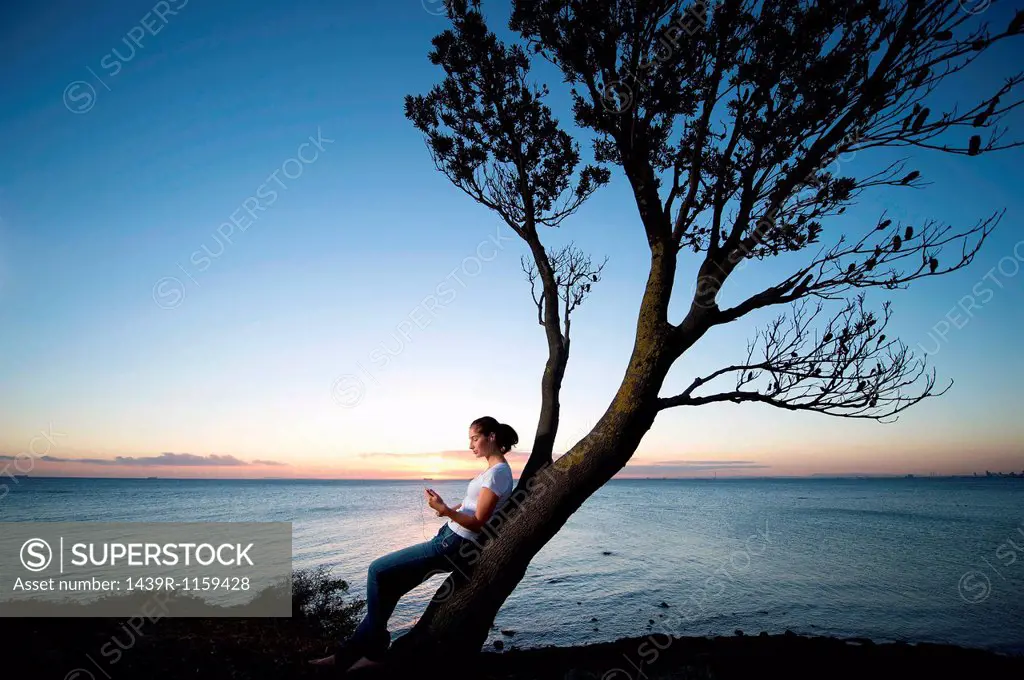 Young woman leaning on tree at dusk