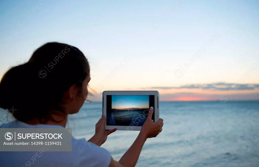 Young woman photographing with her digital tablet at sunset