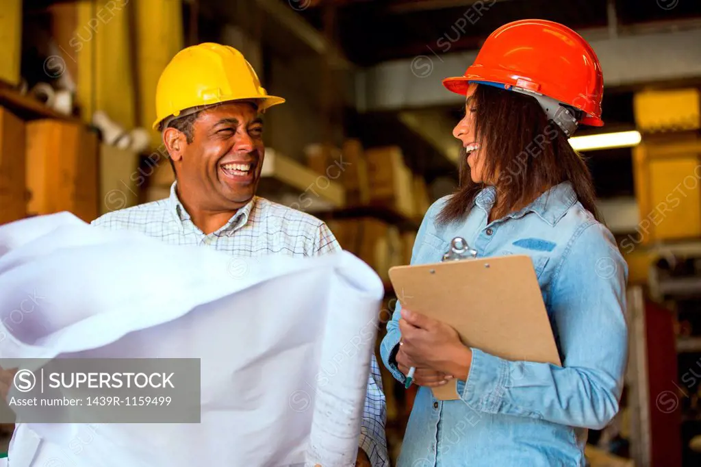 Man and woman in warehouse holding blueprint and clipboard