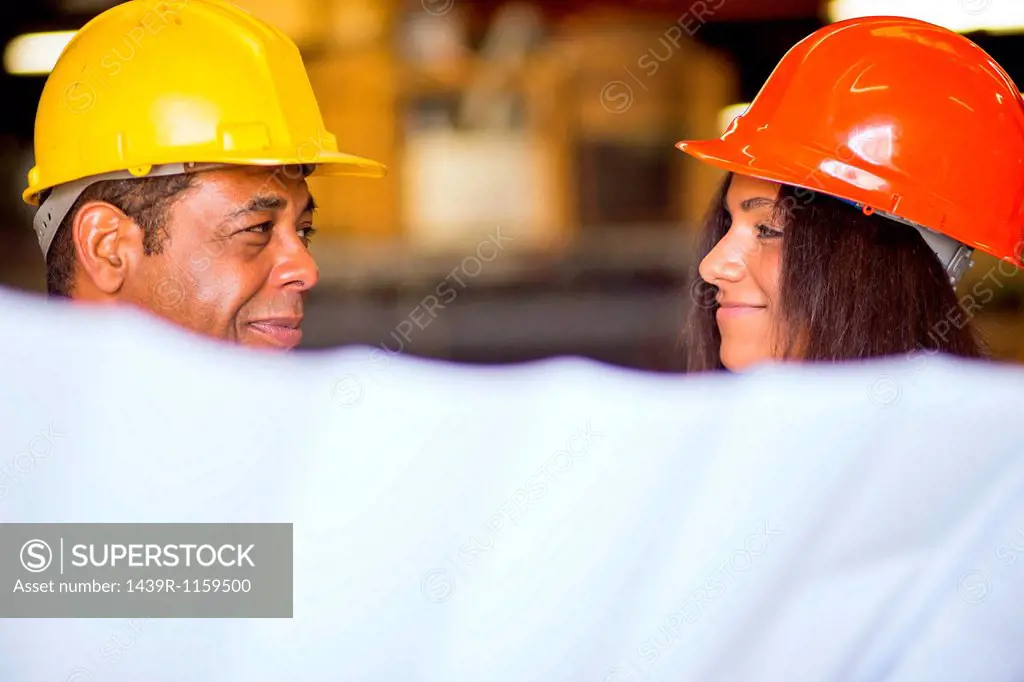 Man and woman in warehouse holding blueprint