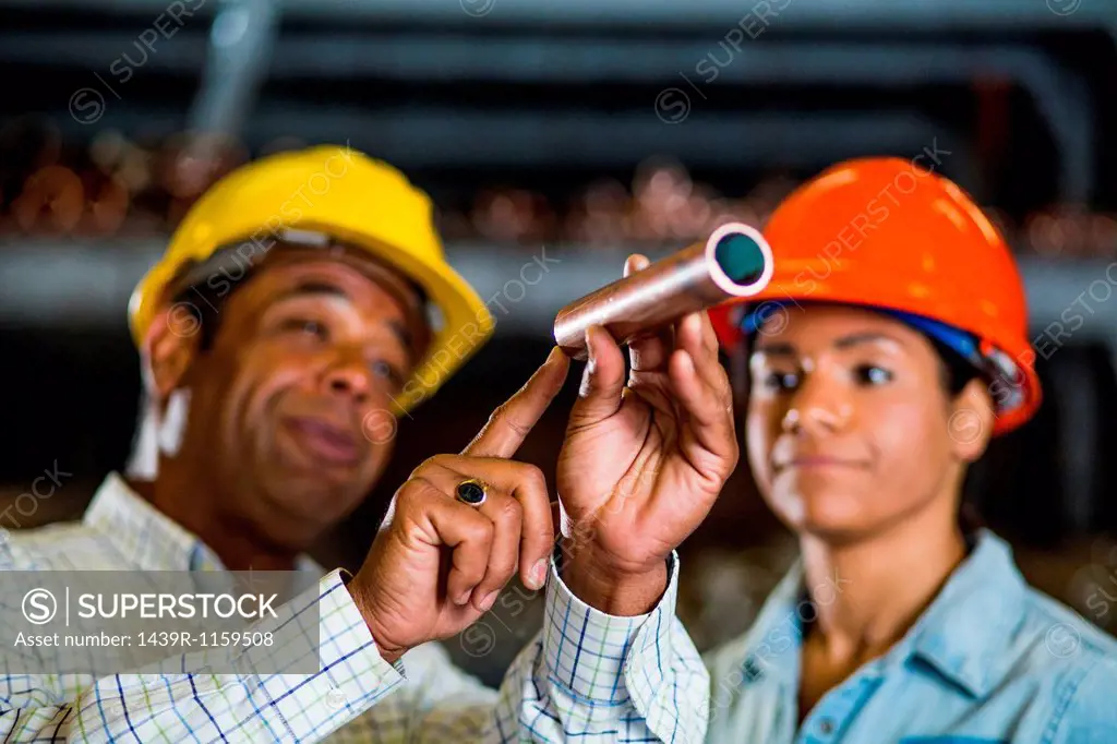 Two warehouse workers inspecting at copper pipe