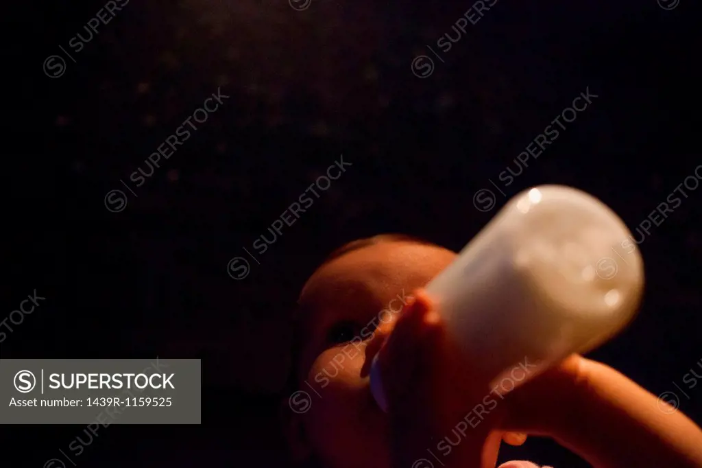 Baby girl feeding from bottle in darkness