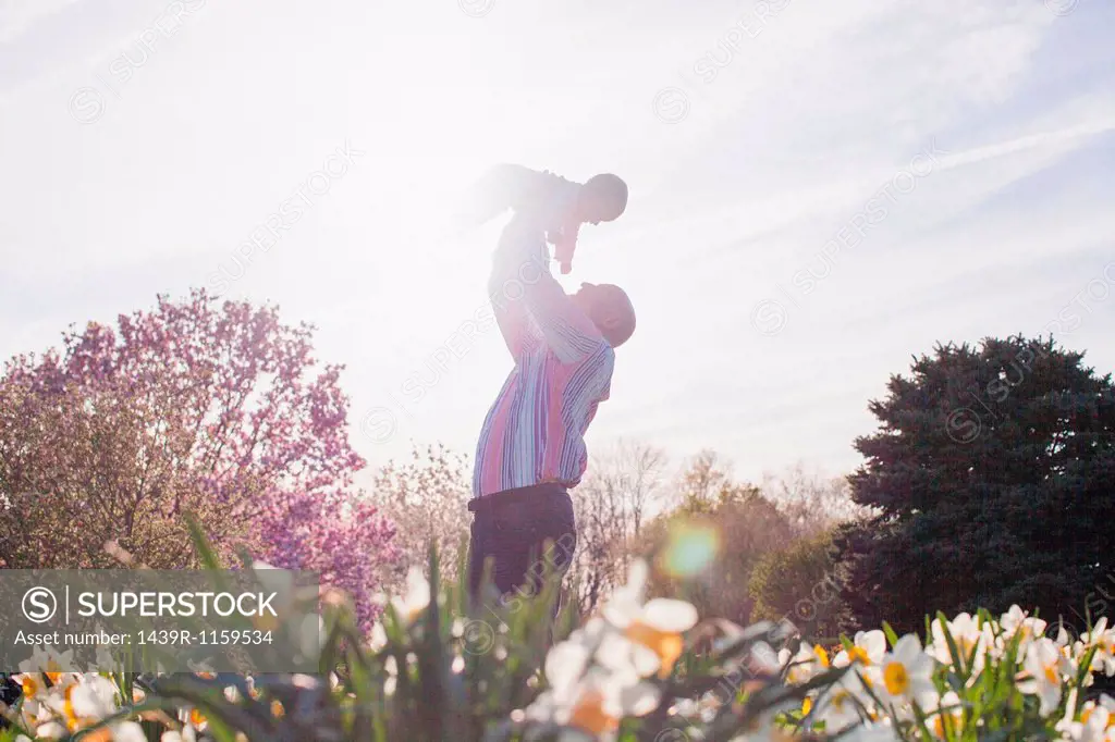 Grandfather holding up granddaughter in garden