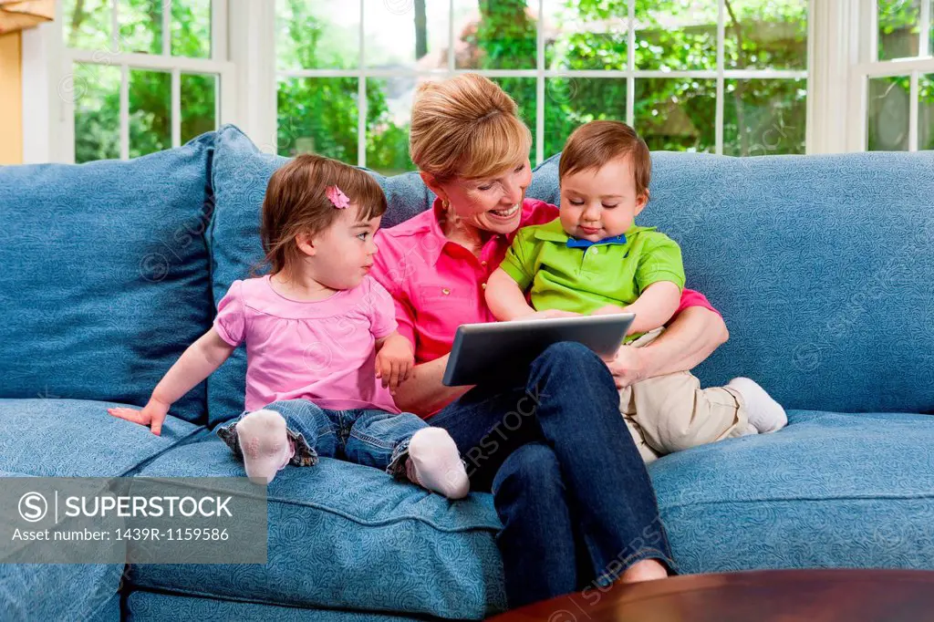 Grandmother and grandchildren on sofa looking at digital tablet