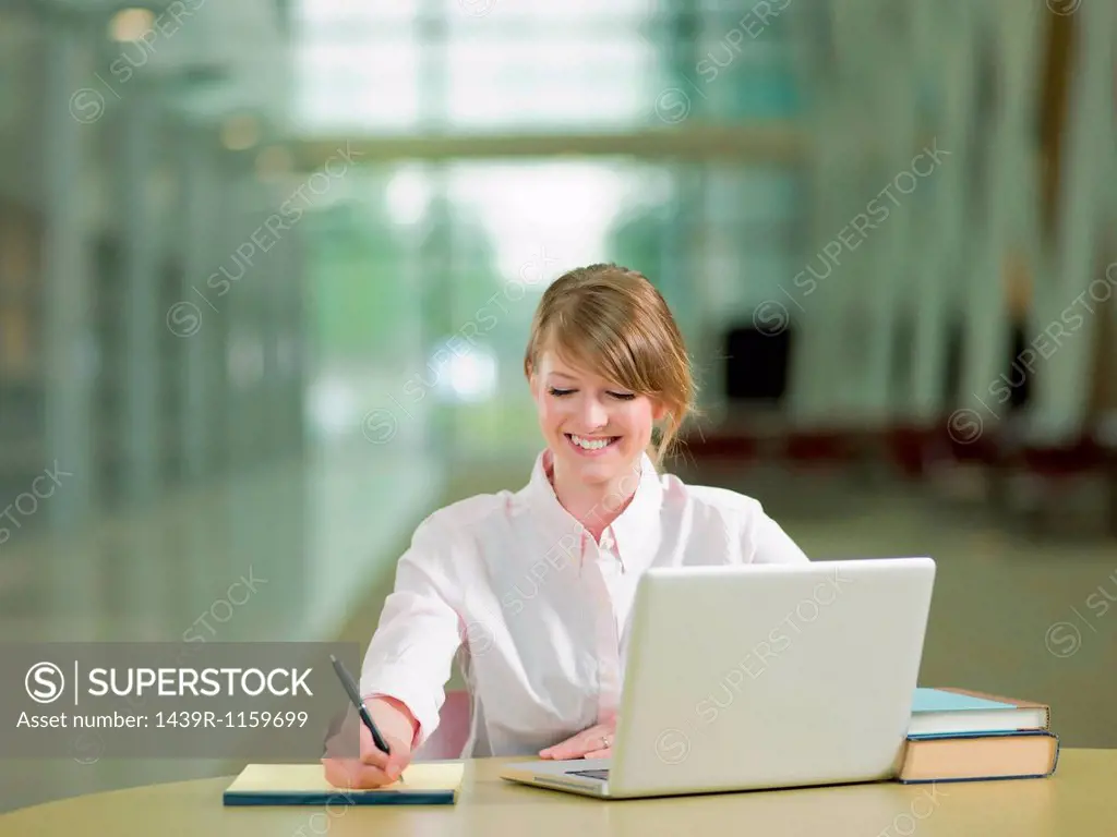 Young student studying taking notes and using laptop, smiling