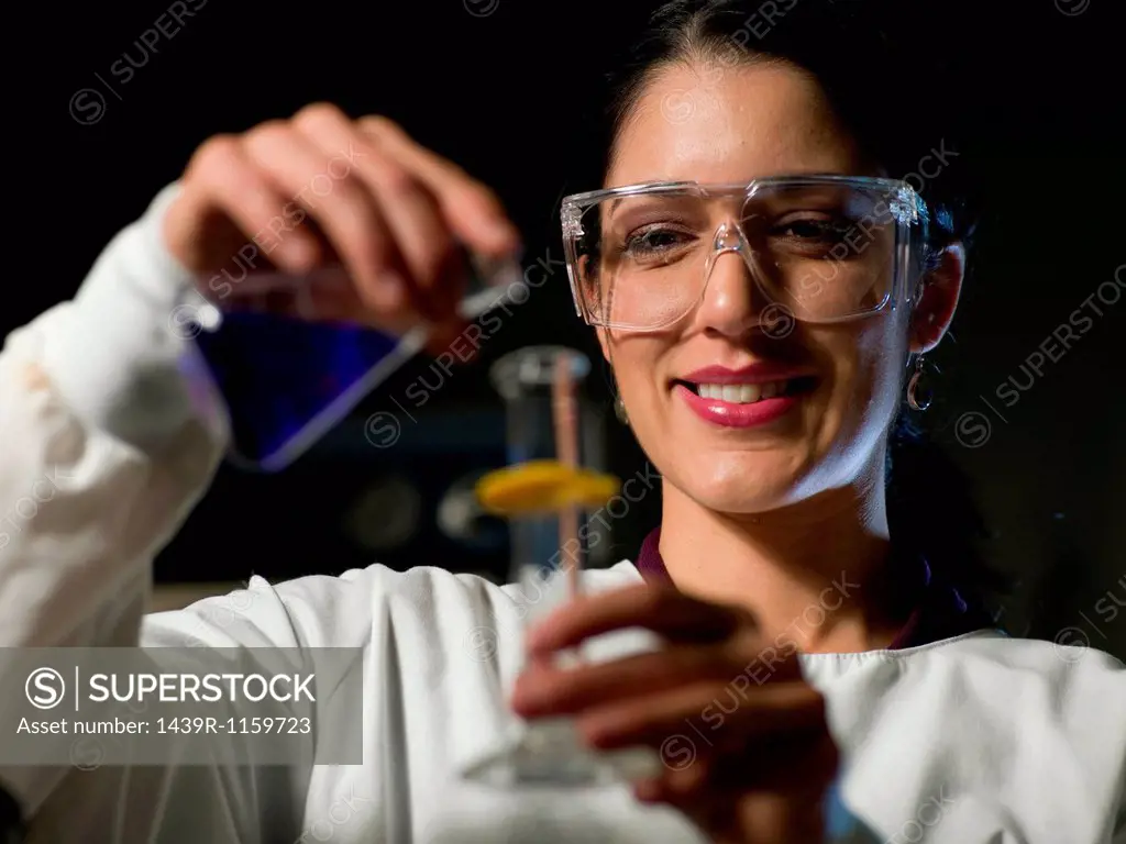 Young scientist in safety glasses mixing chemicals, smiling
