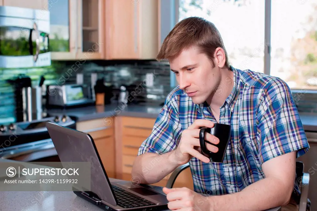 Mid adult man using laptop in kitchen