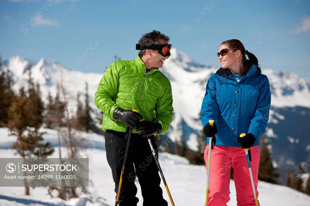 Young woman and mature man in skiwear holding ski poles