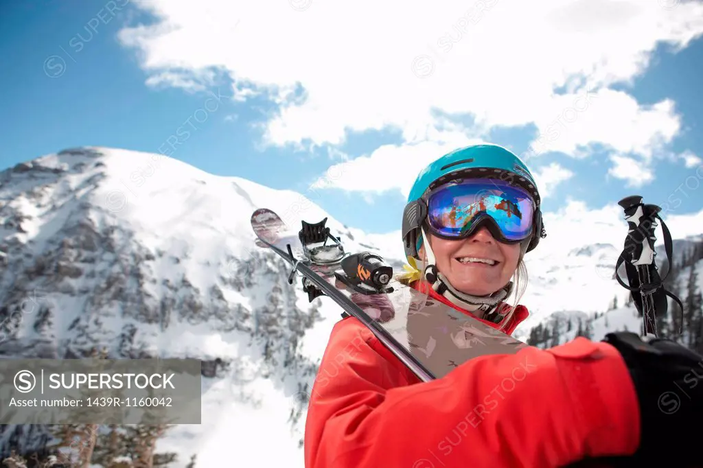 Young woman in skiwear holding skis over shoulder, smiling
