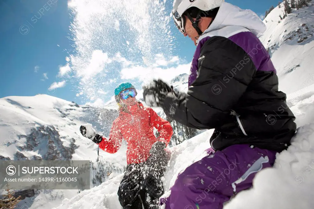 Mid adult man and young woman in skiwear having snowball fight