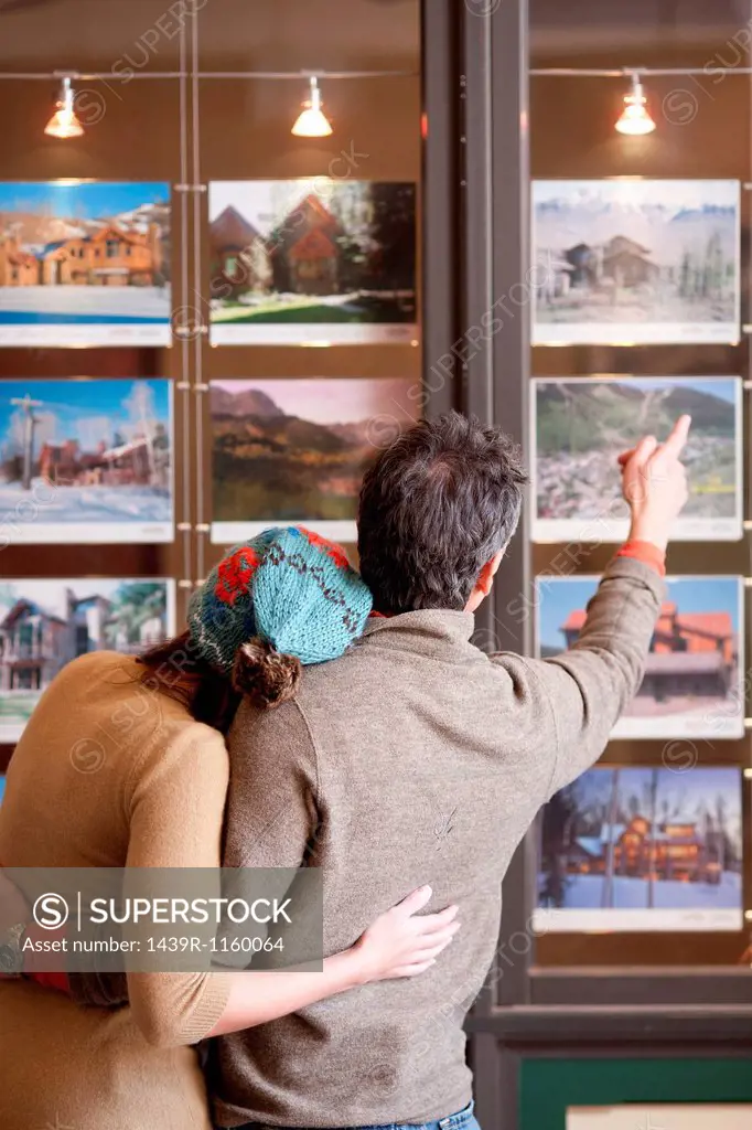 Couple looking at photographs in travel agents window, rear view