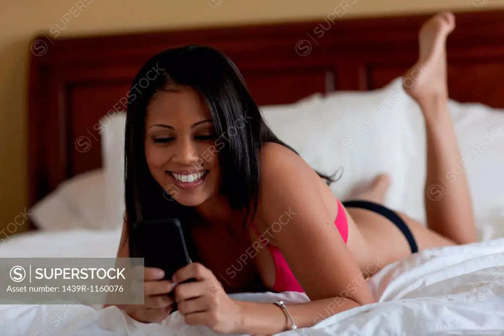 Young woman lying on bed in underwear looking at cellphone
