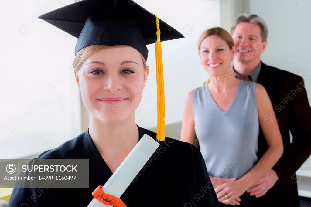 Teenage girl wearing mortarboard with parents in background