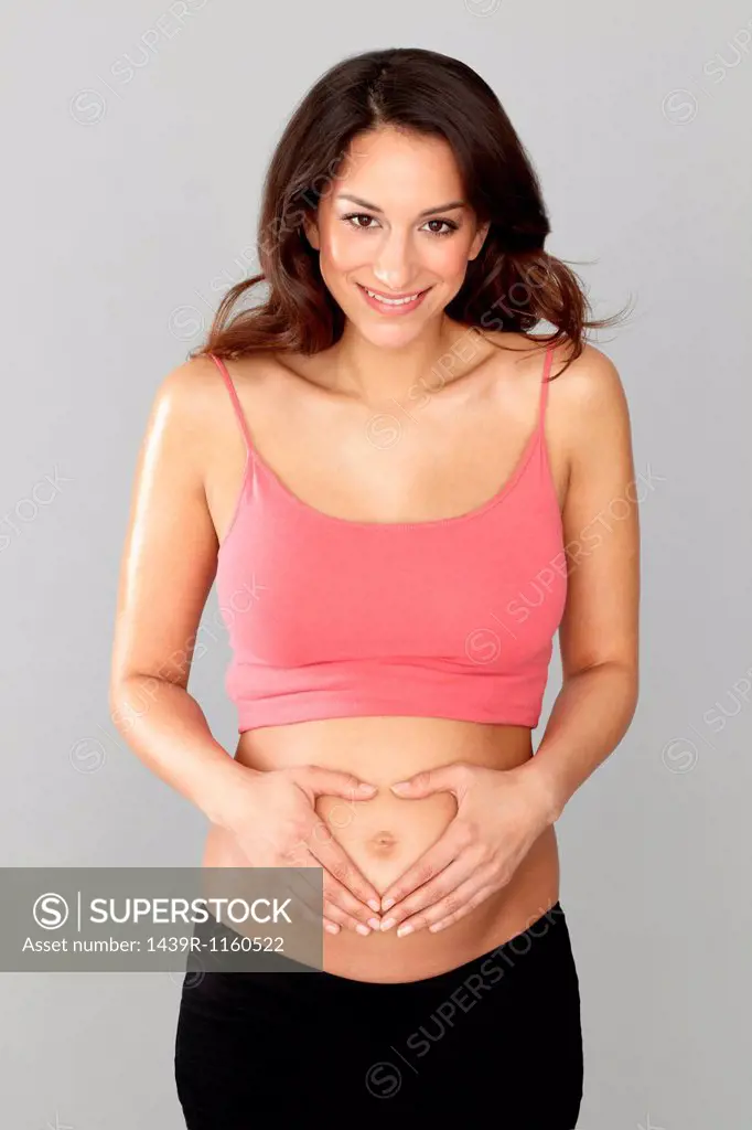 Pregnant woman making heart shape with hands on stomach