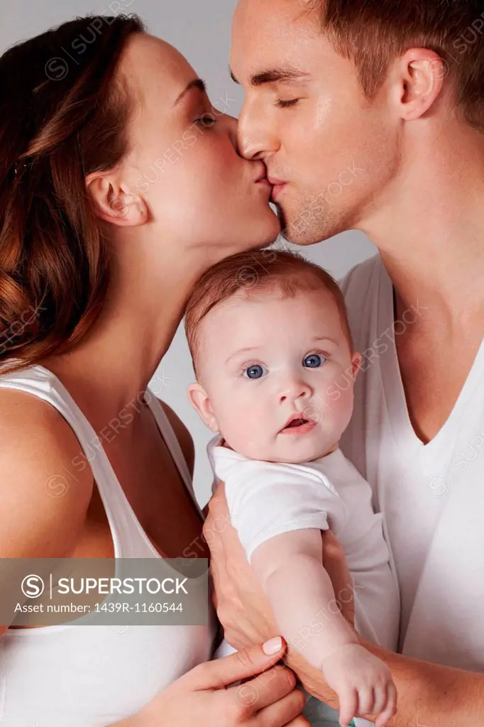 Mother and father kissing, with baby daughter