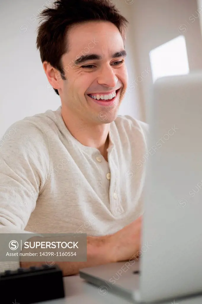 Mid adult man using laptop, laughing